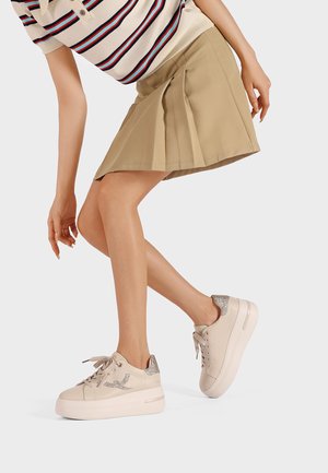 Sneakers platform beige con accenti argentati luccicanti, abbinati a una gonna plissettata beige. Il design presenta una texture liscia e una punta tonda.