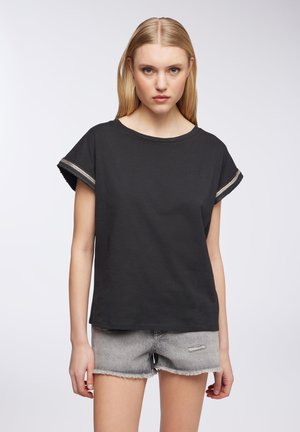 Maglietta nera a maniche corte con scollatura rotonda e dettagli metallici rigati sui polsini. Abbinata a pantaloncini in denim grigi.