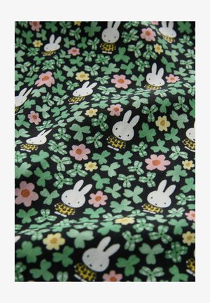 Tissu noir présentant un motif répétitif de lapins blancs, de fleurs dans des teintes de rose et de jaune, et de trèfles verts avec des accents à carreaux.
