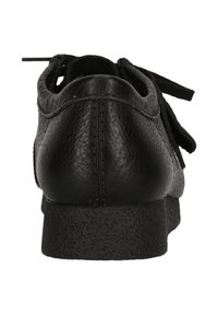 Musta nahkakenkä, jossa on teksturoitu pinta, pyöreä muoto ja kumipohja. Sisältää sidottavat nauhat ja minimalistisen muotoilun.