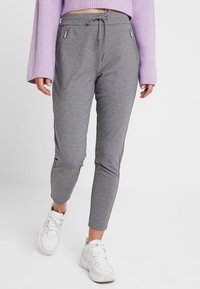 Grå joggingsbyxor med elastisk midja, dragsko och två fickor med dragkedja. Slät textur och slim fit, matchat med vita sneakers.