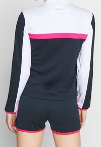 Navy and white athletic top with pink accents, featuring long sleeves and a high collar, paired with navy shorts with pink trim.