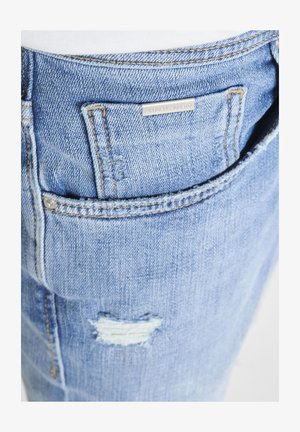 Džep svijetloplavih traperica sa malim metalnim natpisom marke i istrošenim komadićem tkanine ispod džepa.