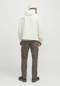 Chaqueta clara con capucha y un logo en la parte trasera, combinada con pantalones cargo oscuros que tienen bolsillos laterales y calzado negro.