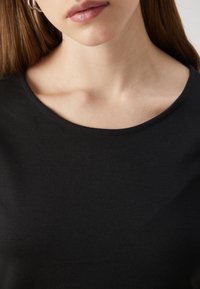 Svart bomullst-shirt med rund hals, slät textur och åtsittande design, som visar endast kragen och övre bröstområdet.