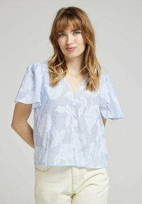 Blouse bleu clair à manches courtes avec motif floral, col en V et fermeture à boutons, en tissu doux et léger avec un léger motif rayé.