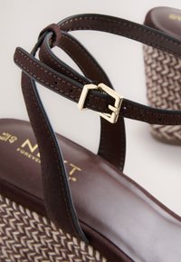 Sandale maro cu bretele, cu talpă platformă împletită și detaliu cu cataramă aurie. Talpă din piele netedă cu branding subtil vizibil. Accente texturate prezente.