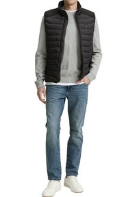 Chaleco negro acolchado con diseño acolchado, suéter gris, vaqueros azules y zapatillas blancas. Cuenta con cuello alto y cierre de cremallera.