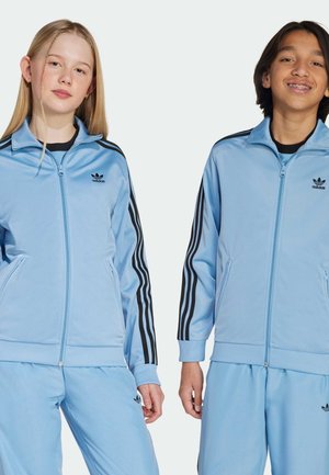 Svijetloplave jakne za trčanje na zatvarač s crnim trostrukim trakama na rukavima. Ima rebraste manžetne i mali Adidas logo na prsima.