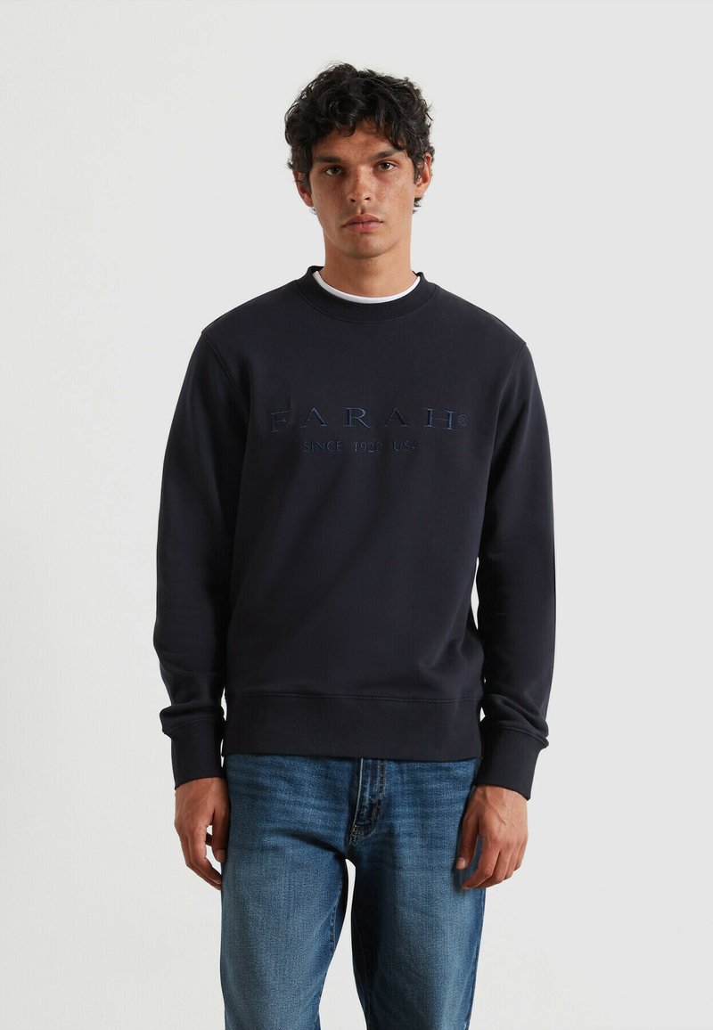 Marine crewneck sweatshirt met geborduurd merkl logo, geribbelde manchetten en onderkant, gemaakt van zachte stof, gedragen over blauwe jeans.