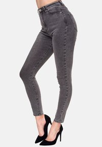 Jeans ajustados de talle alto grises con una textura suave, que cuentan con presillas para cinturón, bolsillos delanteros y un cierre con un solo botón, combinados con tacones negros.