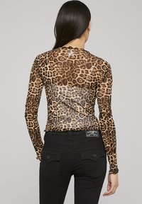 Pitkittykuvioinen pitkähihaisen läpikuultavasta kankaasta; siinä on istuva malli, laineileva helma ja se sopii yhteen mustien istuvien housujen kanssa.