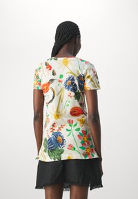 Camiseta de manga corta en algodón blanco con un colorido patrón floral que presenta flores rojas, azules y amarillas, sobre un fondo claro.