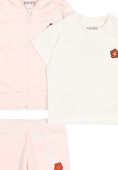 Trzyczęściowy strój dla niemowląt, składający się z jasnoróżowej bluzy z zamkiem, spodni oraz białej koszulki z krótkim rękawem ozdobionej małymi czerwonymi kwiatowymi naszywkami.