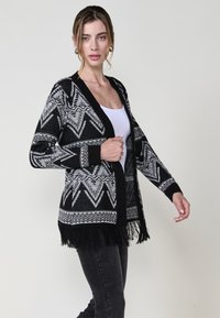 Cardigan a righe bianche e nere realizzato in tessuto a maglia, con orlo frangiato, scollatura a V e design aperto davanti.
