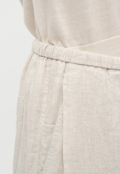 Ρούχο από λινό μπεζ με ελαστική μέση, διαθέτει πιέτες και πλαϊνές τσέπες. Η υφή είναι απαλή και φυσική.