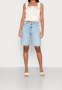 Pletený top na ramínka se čtvercovým výstřihem a vlnkovanými okraji, kombinovaný s světle modrými denims šortkami. Světle béžové sandály na blokovém podpatku doplňují vzhled.