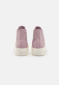 Vysoké tenisky z měkké levandulové kůže s bílou gumovou podrážkou. Disponují logem Converse na patě a texturovaným prošíváním.