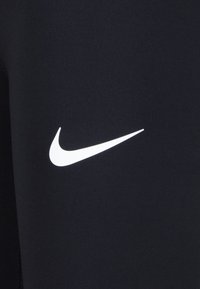 Leggings de sport noirs en tissu extensible, avec un logo Nike en blanc bien visible sur la cuisse. Texture lisse.