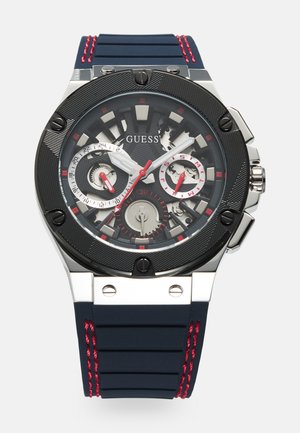 Schwarze und silberne Chronographuhr mit strukturierter Zifferblatt, roten Akzenten und einem navyblauen Gummiband mit roten Stichdetails.