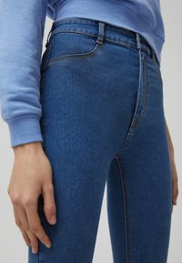 Džíny s vysokým pasem vyrobené z modrého denimového materiálu s hladkým povrchem, obsahující klasický pětizásuvkový design a diskrétní švy podél švů.