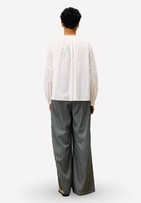 Blouse blanche à manches longues avec dos froncé, associée à un pantalon large à rayures noires et blanches taille haute. Tissu simple et texturé, coupe ample.
