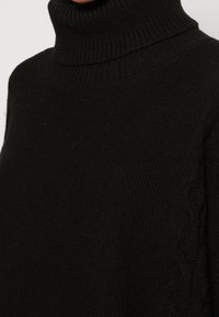 Musta poolne kaelus-svets, mis on valmistatud kudumifilmist, millel on ribitud kaelus ja kettkudumise detailid küljel. Pehme tekstuur.