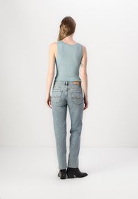 Vaaleansininen ribattu hihaton paita, korkeavyötäröiset vaaleat farkut, joissa on takataskut ja zigzag-ompeleet, yhdistettynä mustiin paksupohjaisiin saappaisiin.