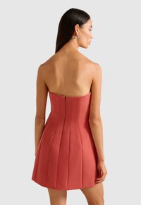 Trägerloses korallenfarbenes Kleid mit vertikalen Falten, tailliertem Oberteil und ausgestelltem Rock. Seitenreißverschluss, aus glattem Stoff mit matter Oberfläche gefertigt.