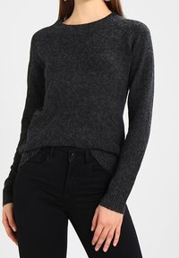 Dunkelgrauer Strickpullover mit rundem Halsausschnitt, langen Ärmeln, strukturierter Oberfläche und lockerer Passform, kombiniert mit schwarzen Jeans.