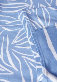 Tissu bleu clair présentant un motif de feuilles blanches, texture lisse et couture visible le long du bord.