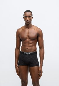 Fekete boxernadrág ismétlődő mintával és fehér Diesel logóval az elasztikus derékpánton. Sima anyagból készült, testhezálló kialakítás.