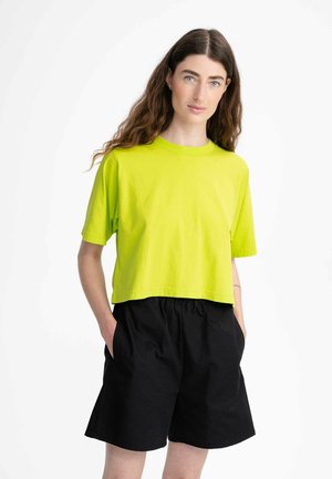 Limoengroen cropped t-shirt van katoen met korte mouwen, gecombineerd met zwarte shorts met elastische taille en zijzakken.