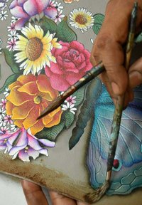 Een hand die twee penselen vasthoudt boven een kleurrijk bloemenschilderij, met heldere bloemen, gedetailleerde texturen en levendige tinten tegen een grijze achtergrond.