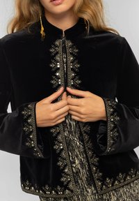 Veste en velours noir avec broderie florale dorée le long du devant et des manches, dotée d'un col montant et d'une fermeture éclair.