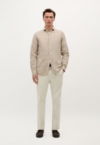 Cămașă băiețească bej deschis cu mâneci lungi, asortată cu pantaloni crem și pantofi maro închis. Design simplu și croi lejer.