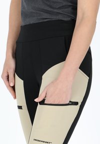 Svart och beige leggings med hög midja, med dragkedjefickor och kontrasterande paneler. Tillverkade av ett mjukt, elastiskt tyg.
