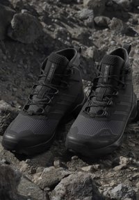Pair of black Adidas Terrex hiking shoes on rocky terrain, designed for outdoor and rough-surface use.