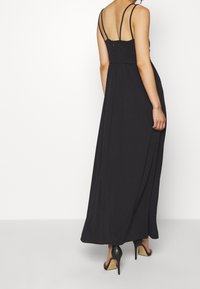 Mustapitu maxi-mekko ohuiden säädettävien olkaimien kanssa, istuva yläosa ja laskostuvahelma, valmistettu sileästä kankaasta. Sisältää takana vetoketjukiinnityksen.