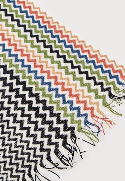 Ύφασμα με πλέξη ζιγκ ζαγκ διαγώνια, με επαναλαμβανόμενα χρώματα: μαύρο, άσπρο, πράσινο, μπλε, πορτοκαλί, μπεζ, και φουντωτές άκρες σε λευκό φόντο.