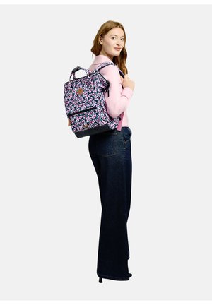 Woman wearing pink sweater and dark jeans carries floral patterned backpack over one shoulder, looking over right shoulder.