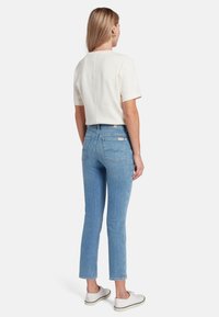 Top corto a maniche corte color crema chiaro, jeans a vita alta blu chiaro, silhouette aderente, leggermente elasticizzati e sneakers bianche. Texture morbida, design minimale.