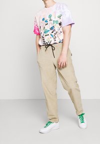 Tričkot s krátkým rukávem v pastelových barvách růžové a fialové s barevnými grafickými potisky, spárované s béžovými, texturovanými kalhotami a bílými teniskami.