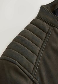 Dunkelgrüner Ledermantelabschnitt mit gestepptem Schulterdetail, glatter Textur und genähten Nähten, die das robuste Design betonen.