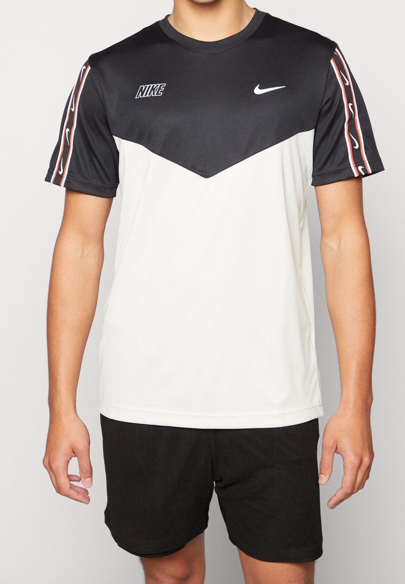 Person som bär en svart-vit Nike sportt-shirt med logotyp på bröstet och randiga mönster på ärmarna, kombinerad med svarta meshshorts.