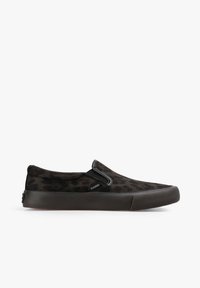 Zapatilla negra tipo slip-on con sutil estampado de leopardo, paneles elásticos en los laterales y suela de goma gruesa, con la etiqueta "Scalpers" en el costado.