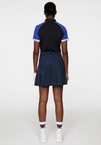 Svart och blå pikétröja med krage, i kombination med en marinblå plisserad kjol med sidodetalj. Vita strumpor och skor fulländar looken.