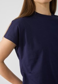 Námořnická modrá bavlněná tričko s kulatým výstřihem a krátkými rukávy, hladká textura a volný střih.