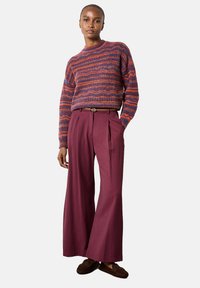 Knit sweater with red, purple, and orange horizontal stripes, paired with wide-leg burgundy trousers. Textured fabric and pleated design.