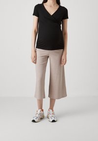 Černý top s krátkými rukávy a zavinovacím designem, doplněný béžovými plisovanými kalhotami a bílými teniskami s oranžovými akcenty.